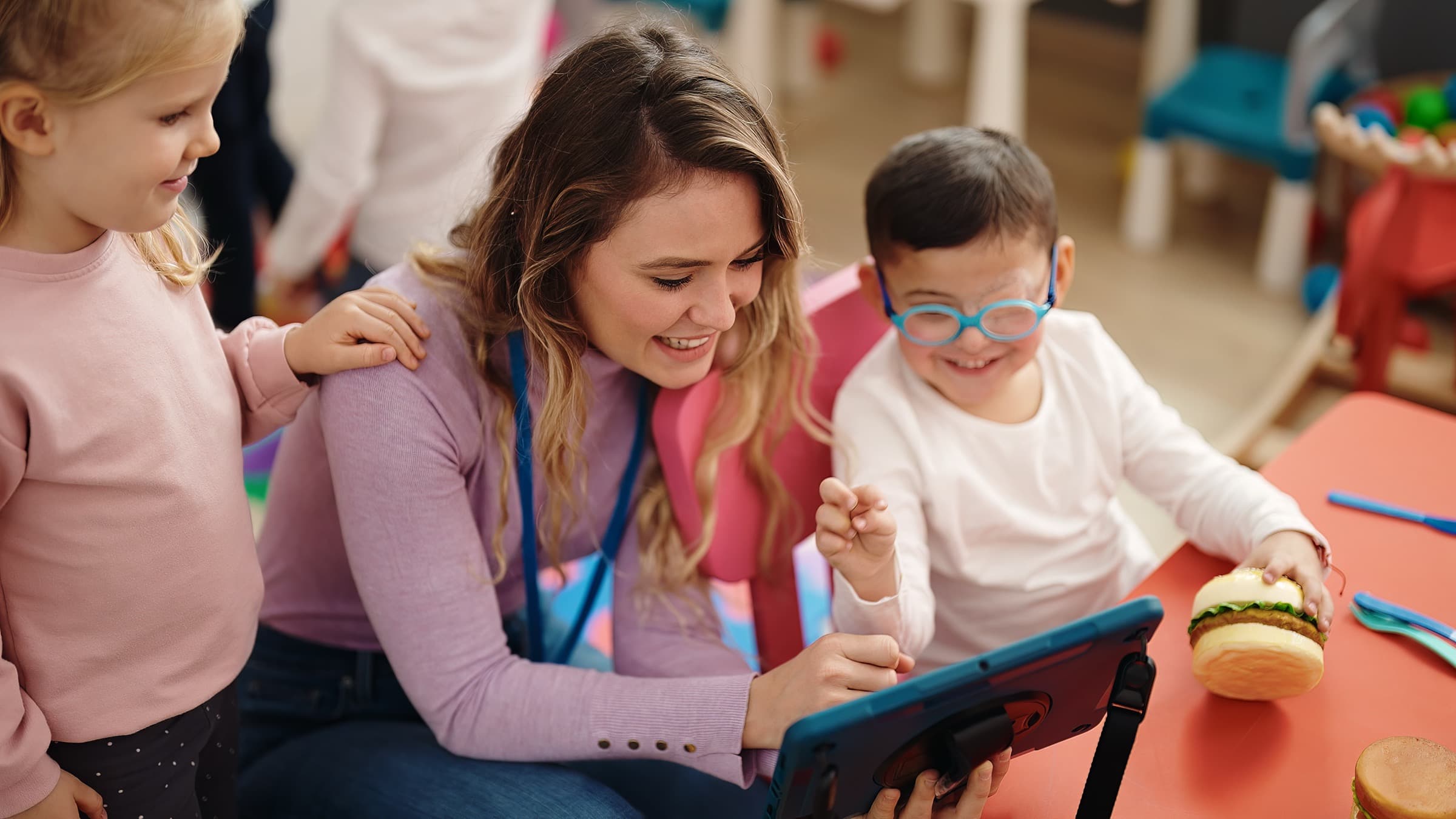 Teacher and two young students sharing a tablet during a phonics activity